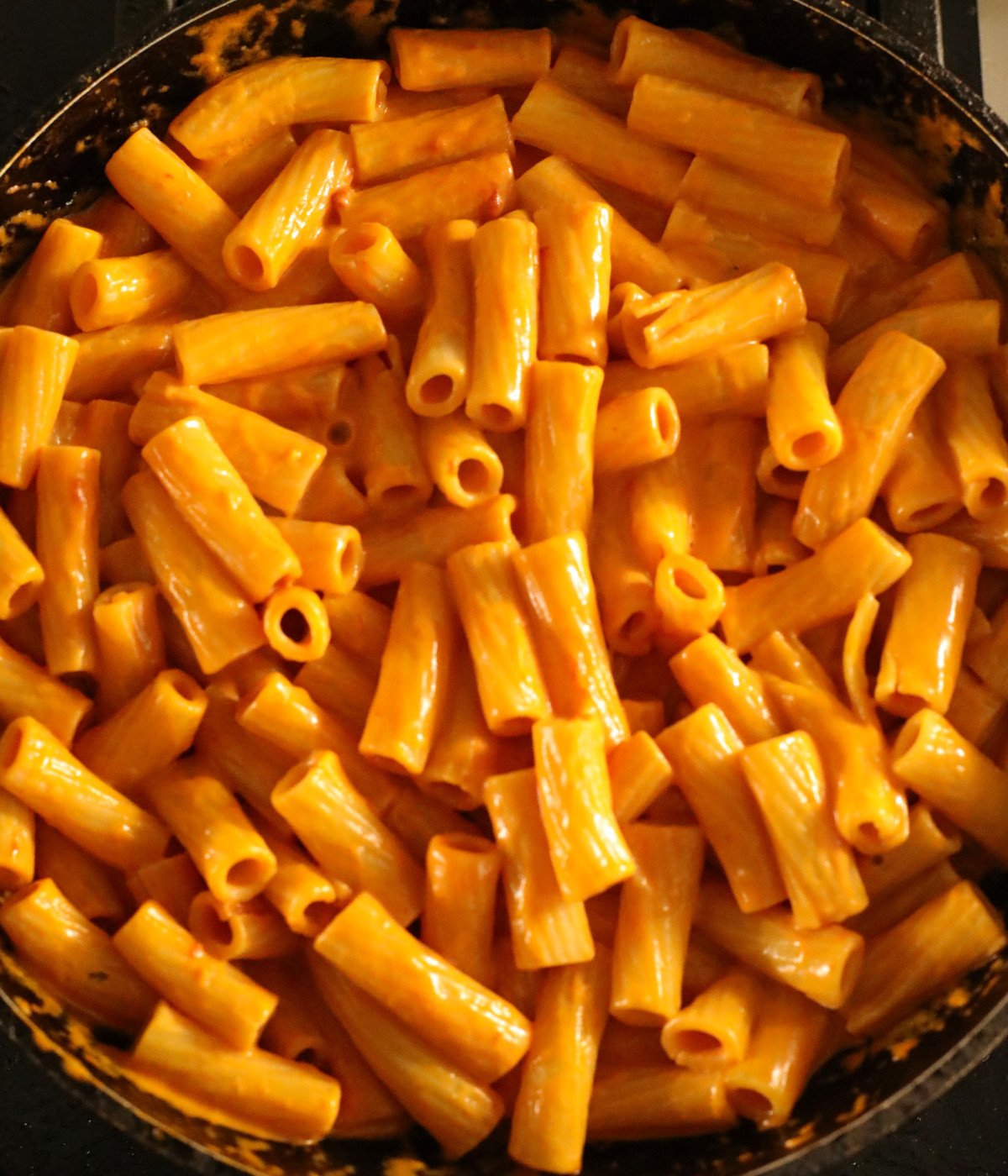 Rigatoni and creamy tomato sauce mixed in a black pan.