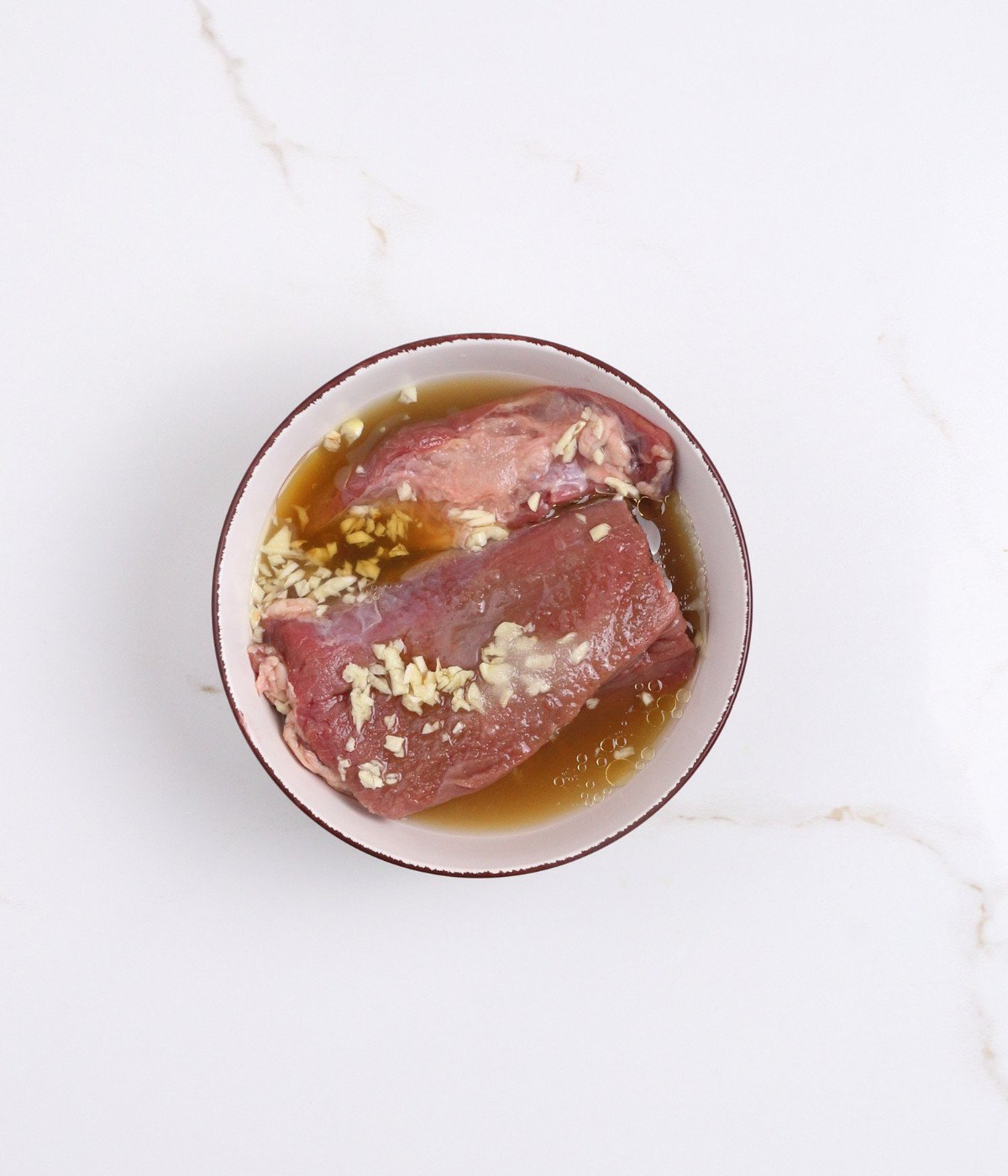 Sirloin steak in marinade with chopped garlic in a bowl.