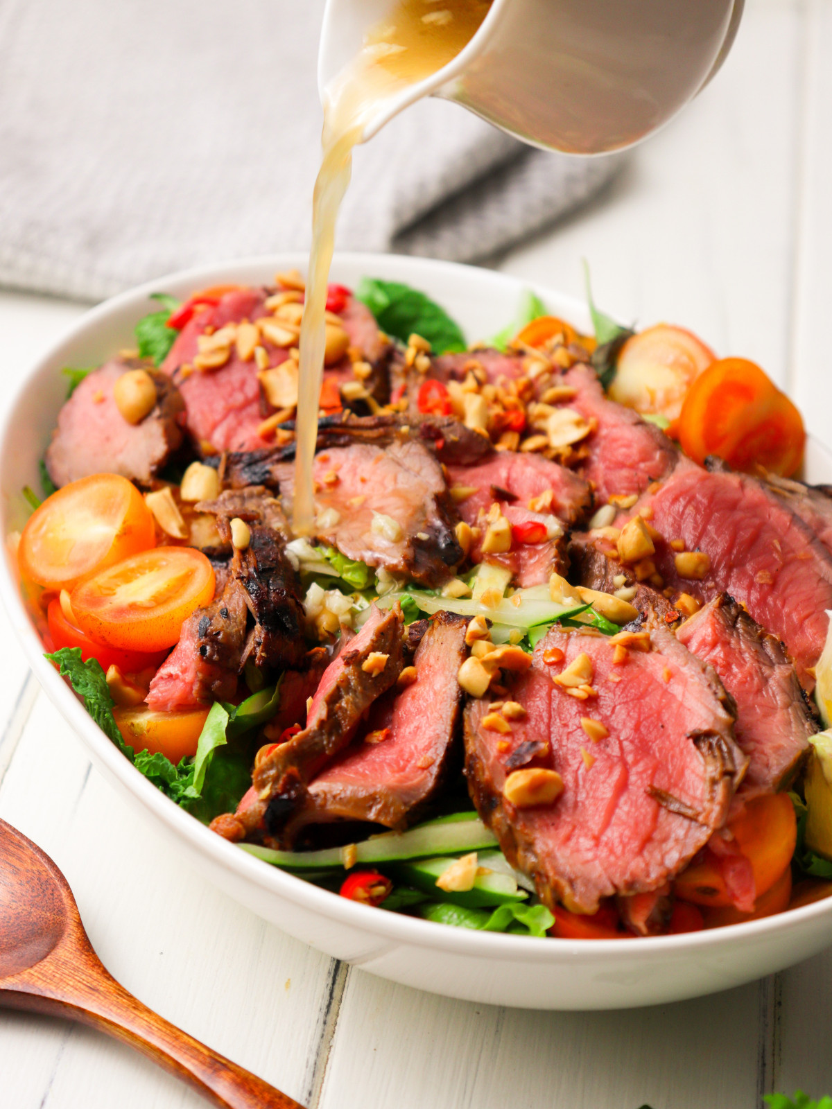 Thai beef salad in a white oval bowl topped with crushed peanuts and a dressing.