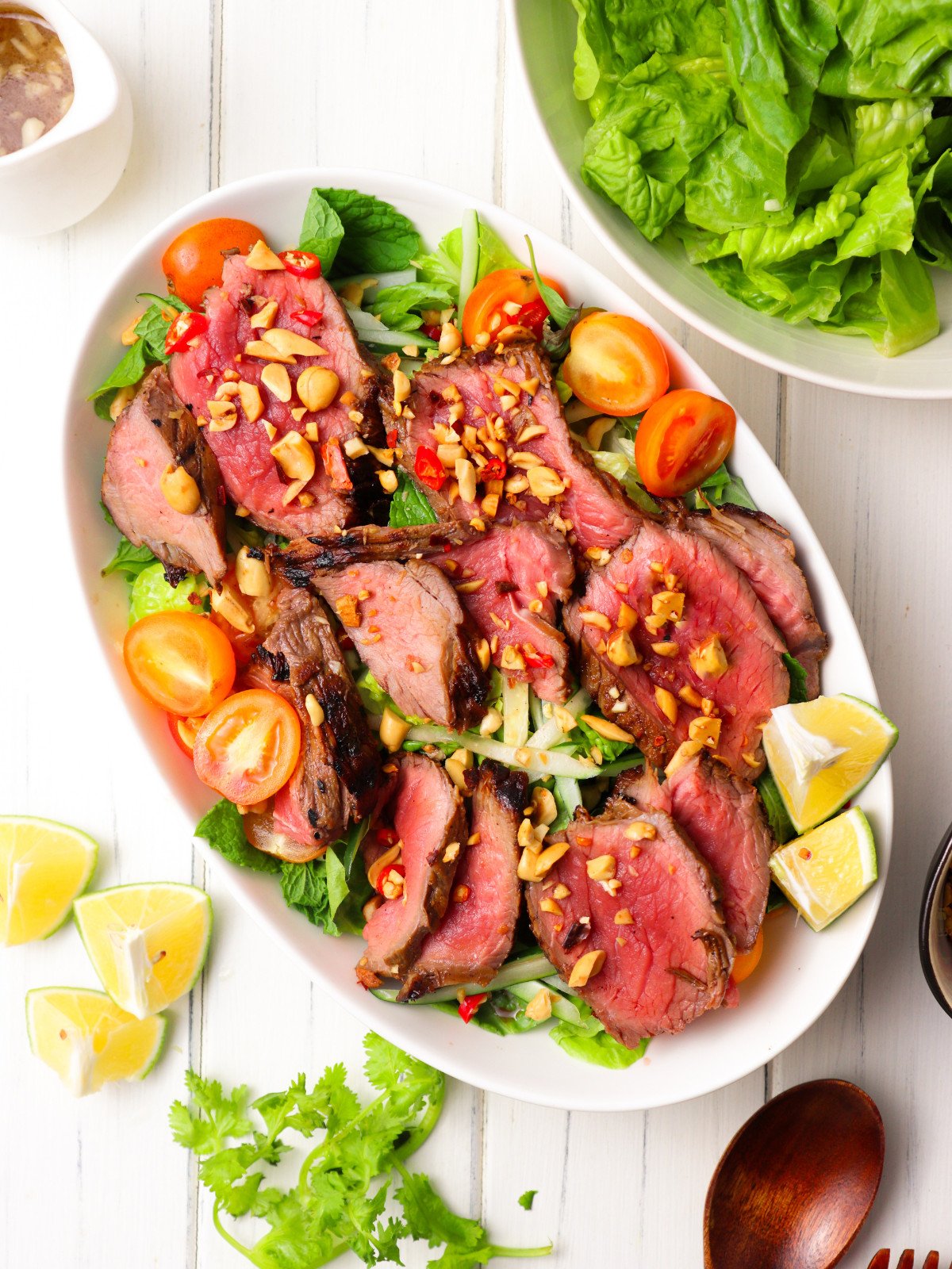 Thai beef salad in a white oval bowl topped with lime and crushed peanuts.