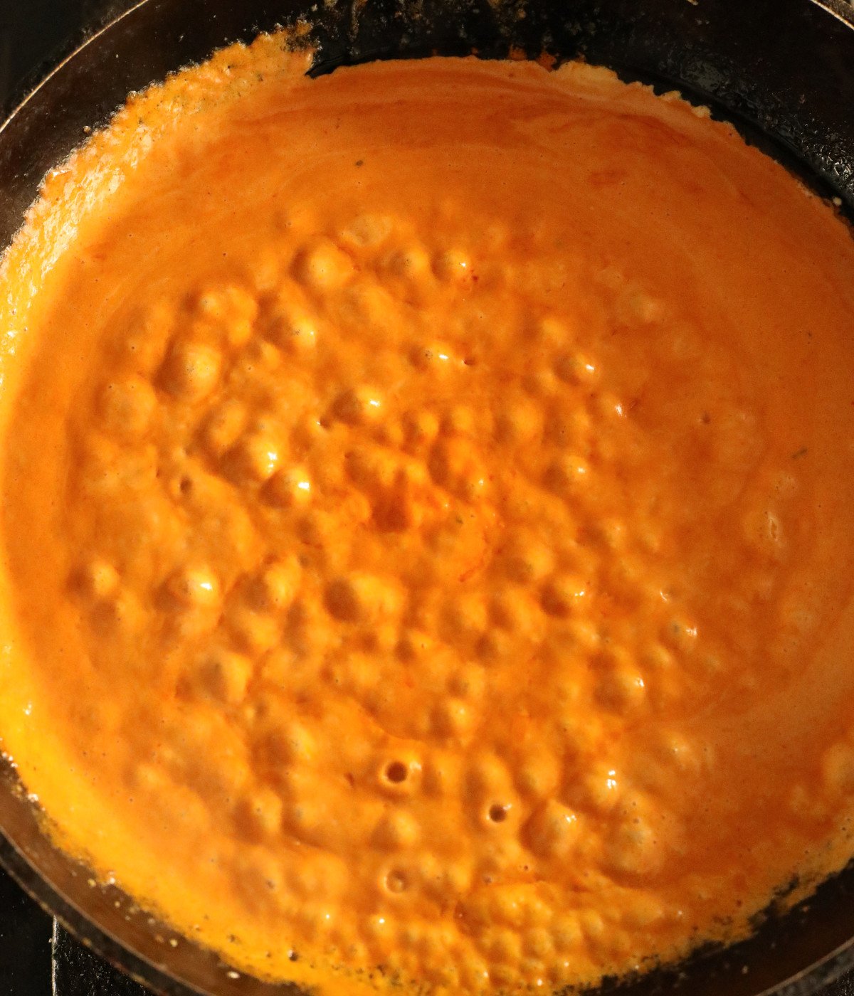 Tomato paste, heavy cream, and seasoning stirred in a black pan.