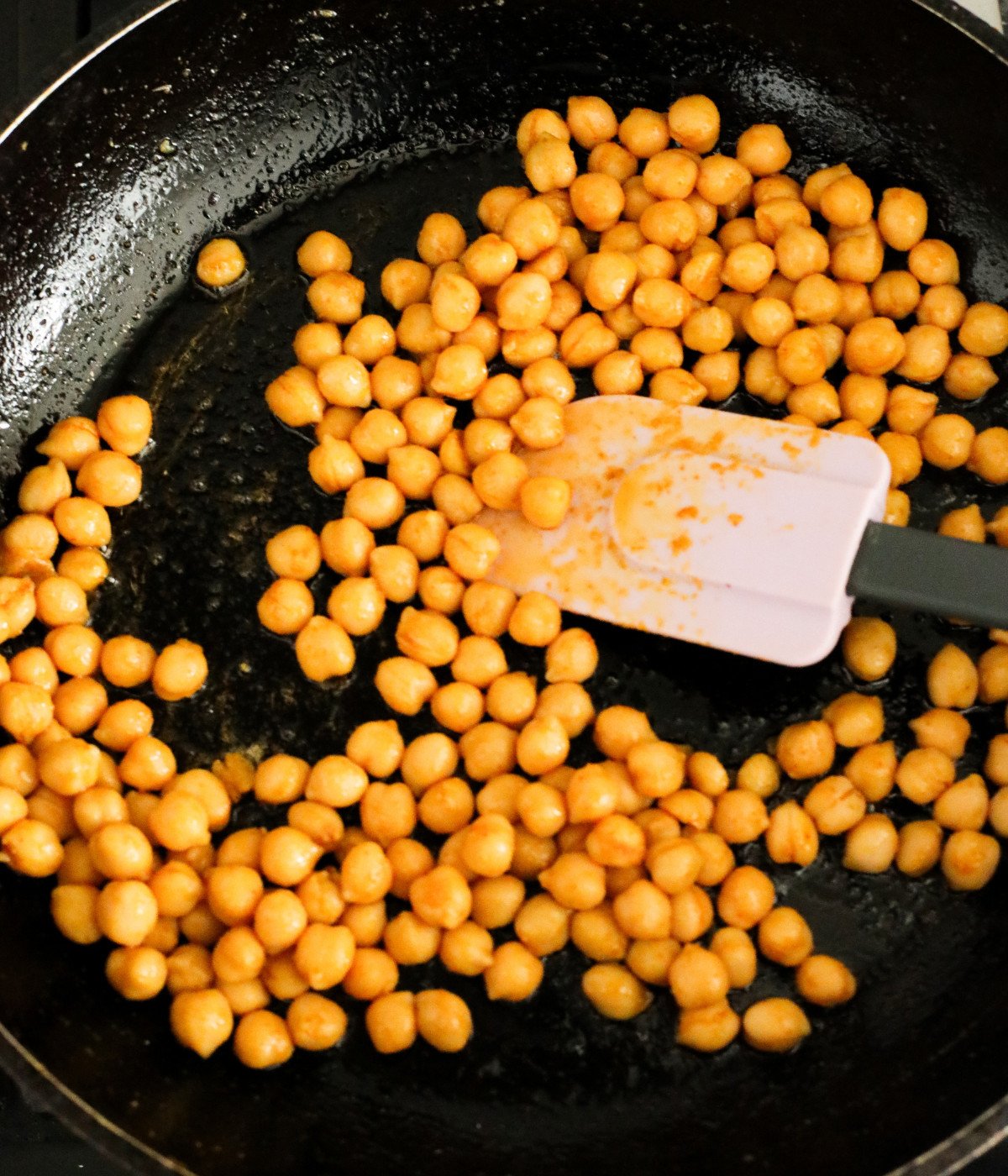 Chickpeas and seasoning mixed in a black pan.