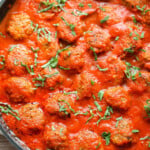 Meatballs in tomato sauce garnished with fresh herbs.