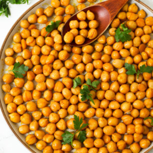 Pan fried chickpeas in a plate with a brown spoon and herbs.