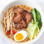 Ramen, beef chunks, pak choi, noodles and boiled egg in a white bowl.