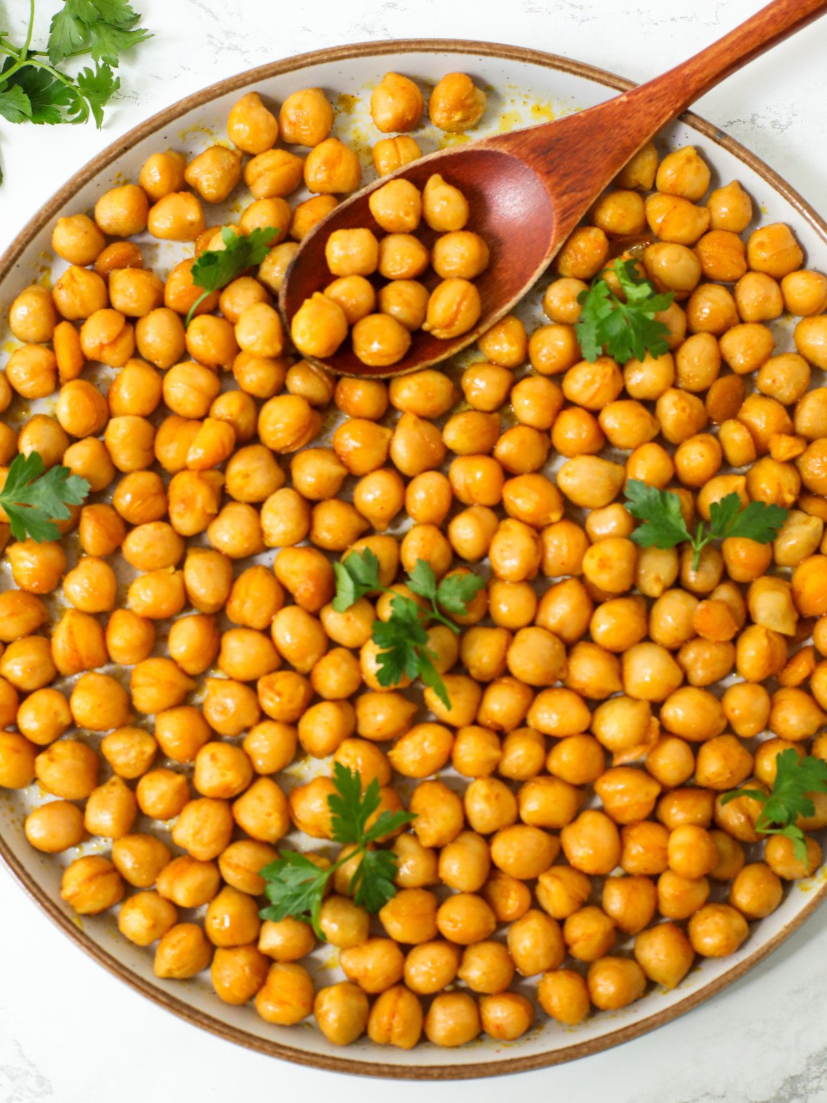Seared chickpeas with herbs on top in a plate with a brown spoon.