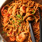 Spicy prawn garlic nodles in a silver wok and black tongs.