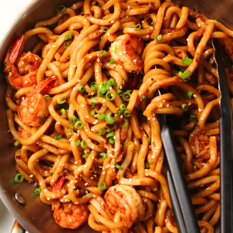 Spicy prawn garlic nodles in a silver wok and black tongs.
