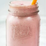 Strawberry and milk mixture in a jar with an orange straw.
