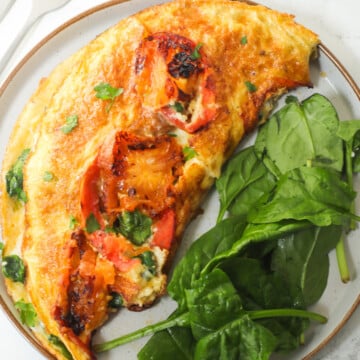 Tomato omelette on a grey plate with baby spinach.