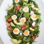 Asparagus, eggs, spinach, tomato, walnuts and radishes on a white plate.