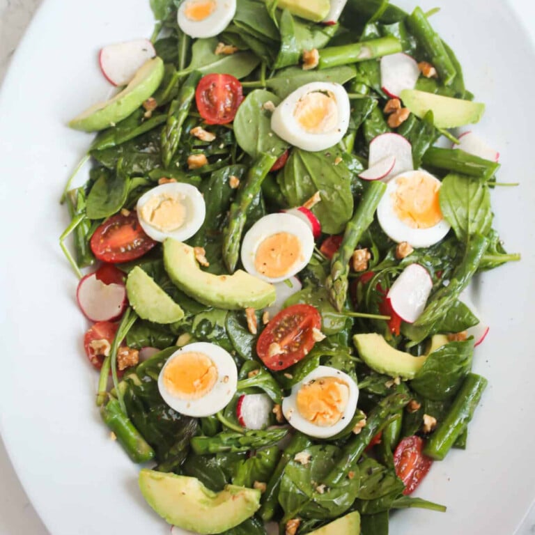 Asparagus, eggs, spinach, tomato, walnuts and radishes on a white plate.