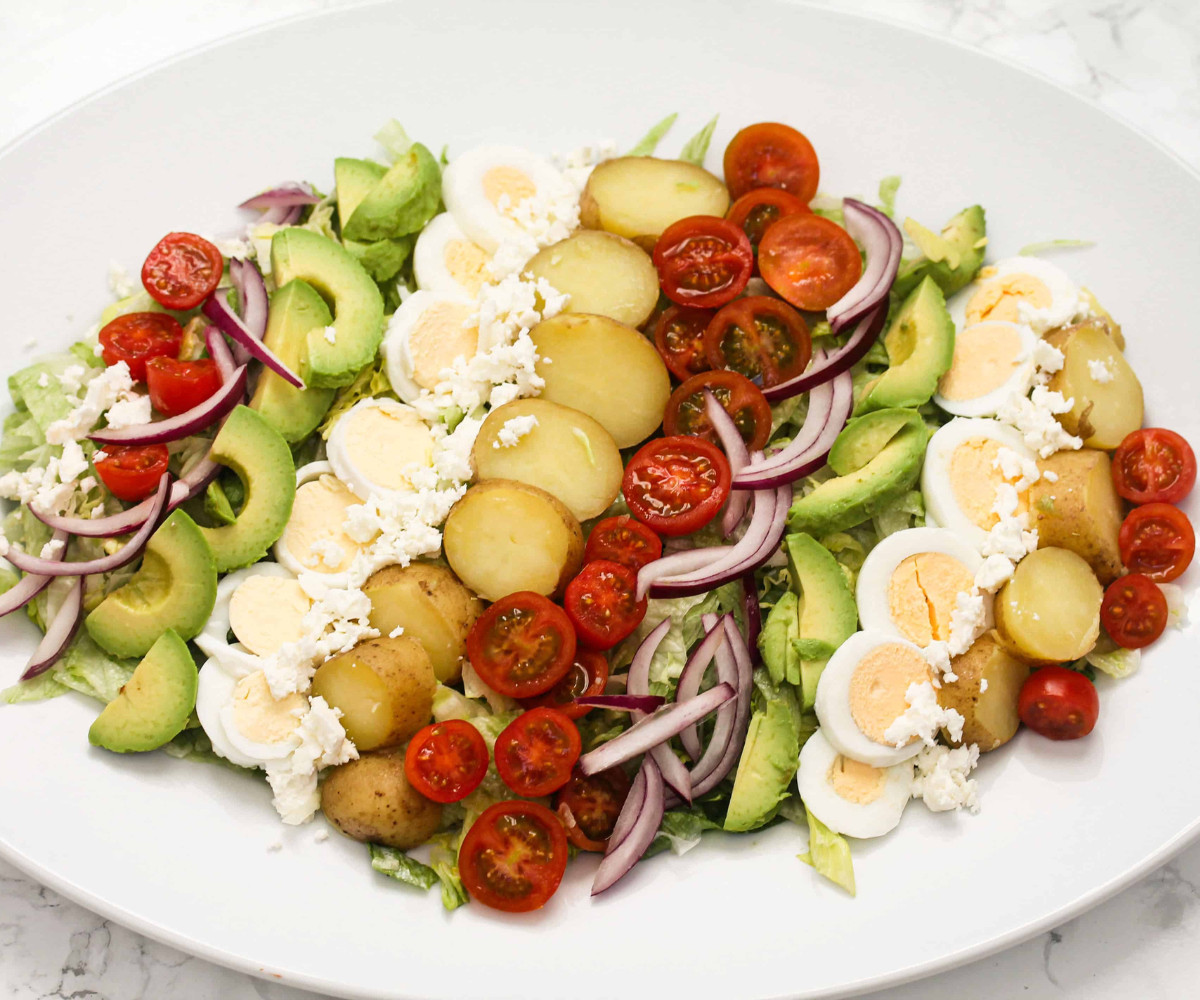 Baby potatoes, avocado, tomato, red onions and boiled egg on a white plate.