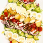 Baby potatoes, tomatoes, boiled eggs, red onions, avocados on a white plate.