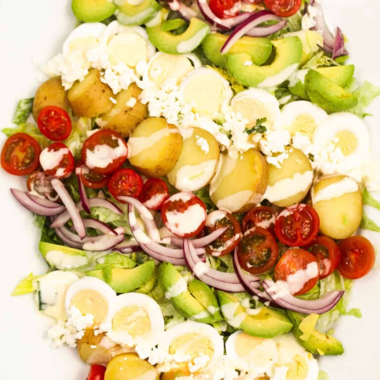 Baby potatoes, tomatoes, boiled eggs, red onions, avocados on a white plate.