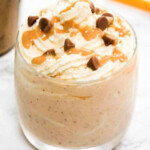 Peanut milkshake in a glass jar with chocolate chips, whipped cream and peanut sauce on top.