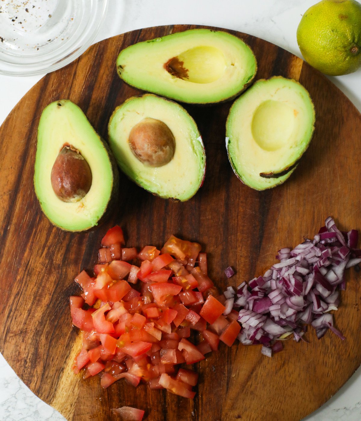 Avocado, diced tomatoes and diced red onions on a wooden board.