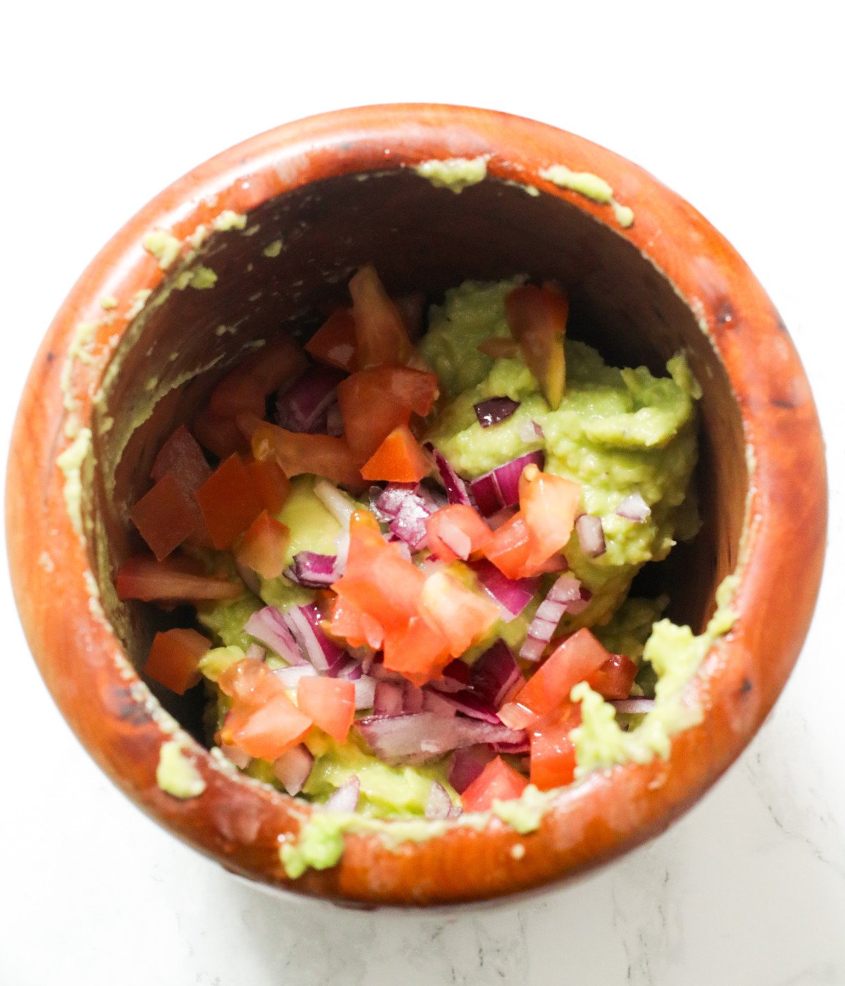 Avocado, diced tomatoes, diced red onions in a brown bowl.