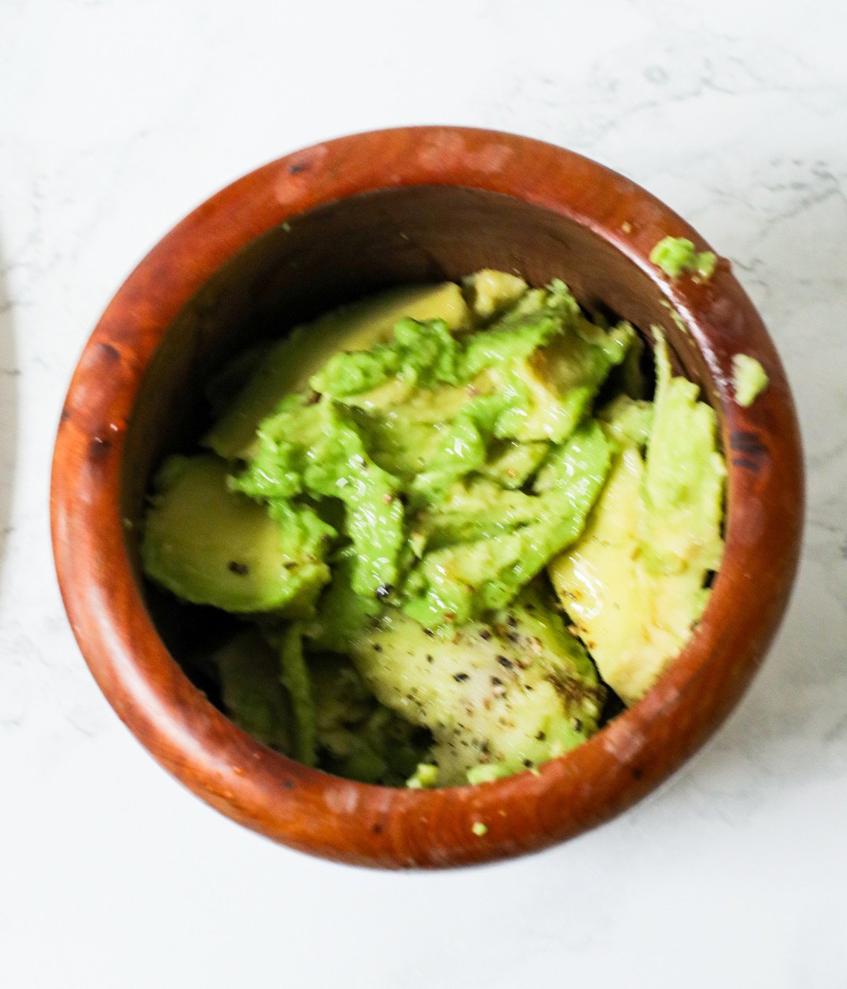 Avocado, salt, black pepper in a brown bowl.