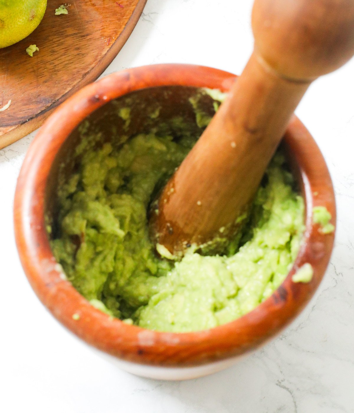 Avocado, salt, black pepper, olive oil and lime crushed in a brown bowl.