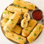 Chinese vegetable spring rolls on a plate with herbs and sweet chili sauce.