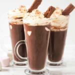 Chocolate drink in three glass cups with marshmallows, whipped cream and chocolate flakes.
