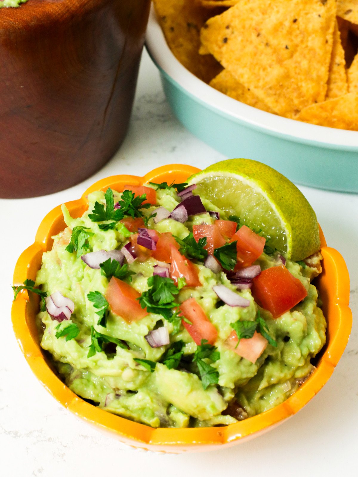 Guacamole with chopped tomatoes, diced red onions, corriander and lime in a bowl. Tortilla chips.