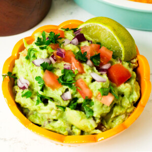 Guacamole with tomatoes, lime and diced red onions in a yellow bowl.
