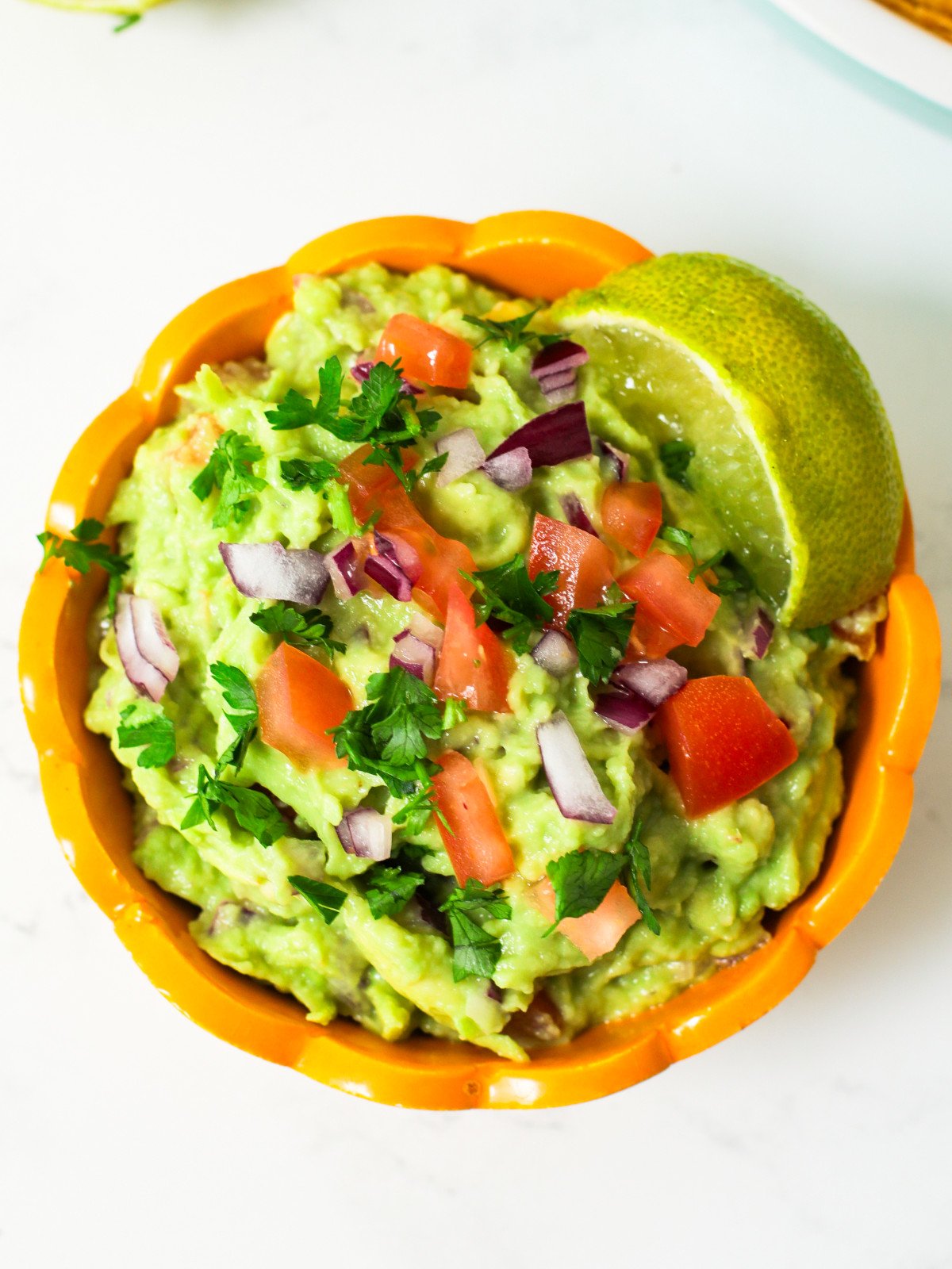 Guacamole with tomatoes, red onions, corriander and lime in a bowl.