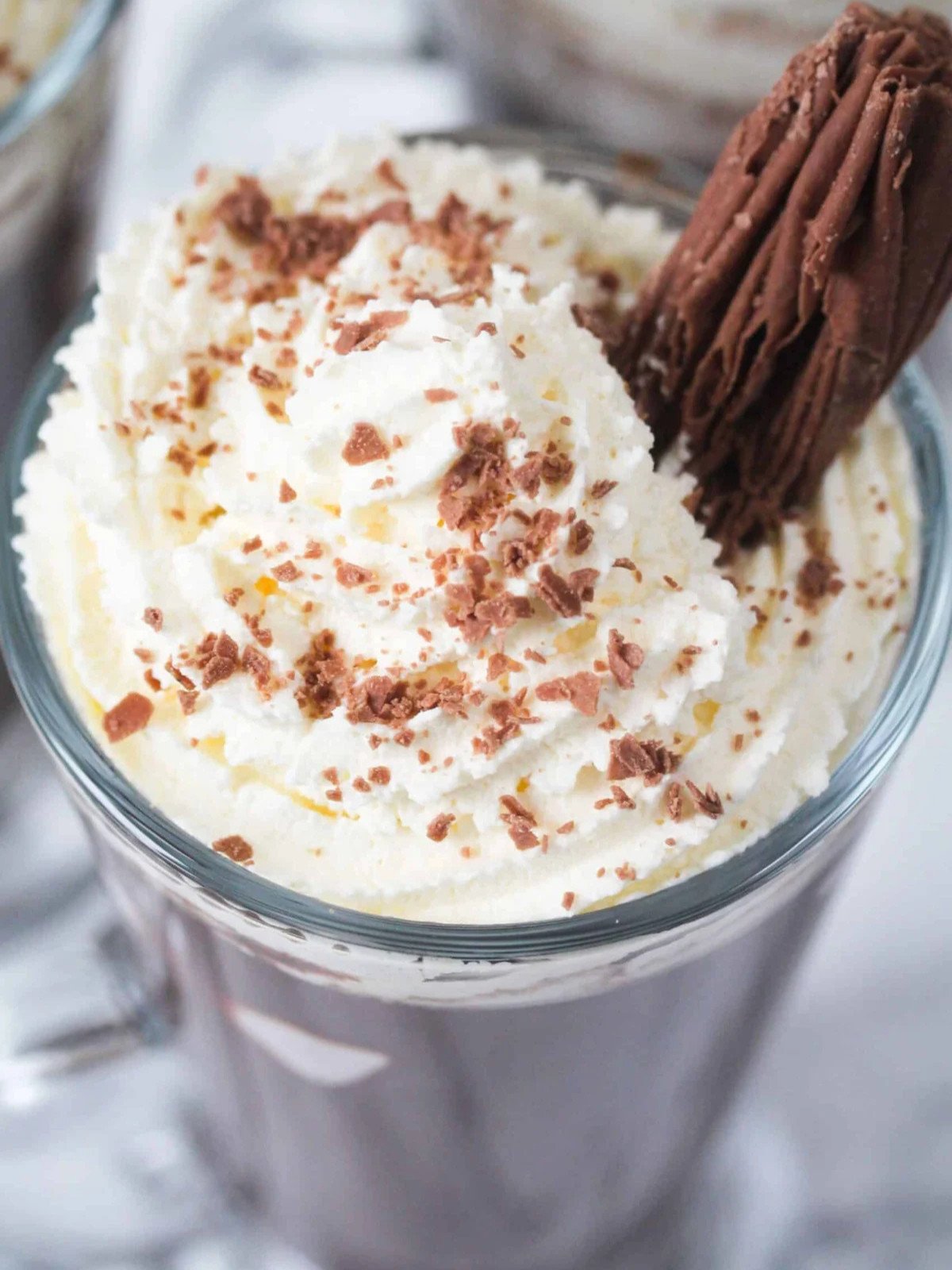 Hot chocolate drink in a glass cup topped with whipped cream, marshmallows and a chocolate flake.
