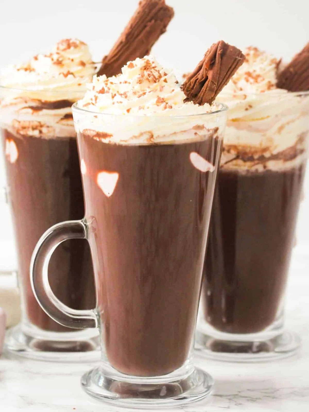 Hot chocolate drink in three glass cups topped with whipped cream, and a chocolate flake.