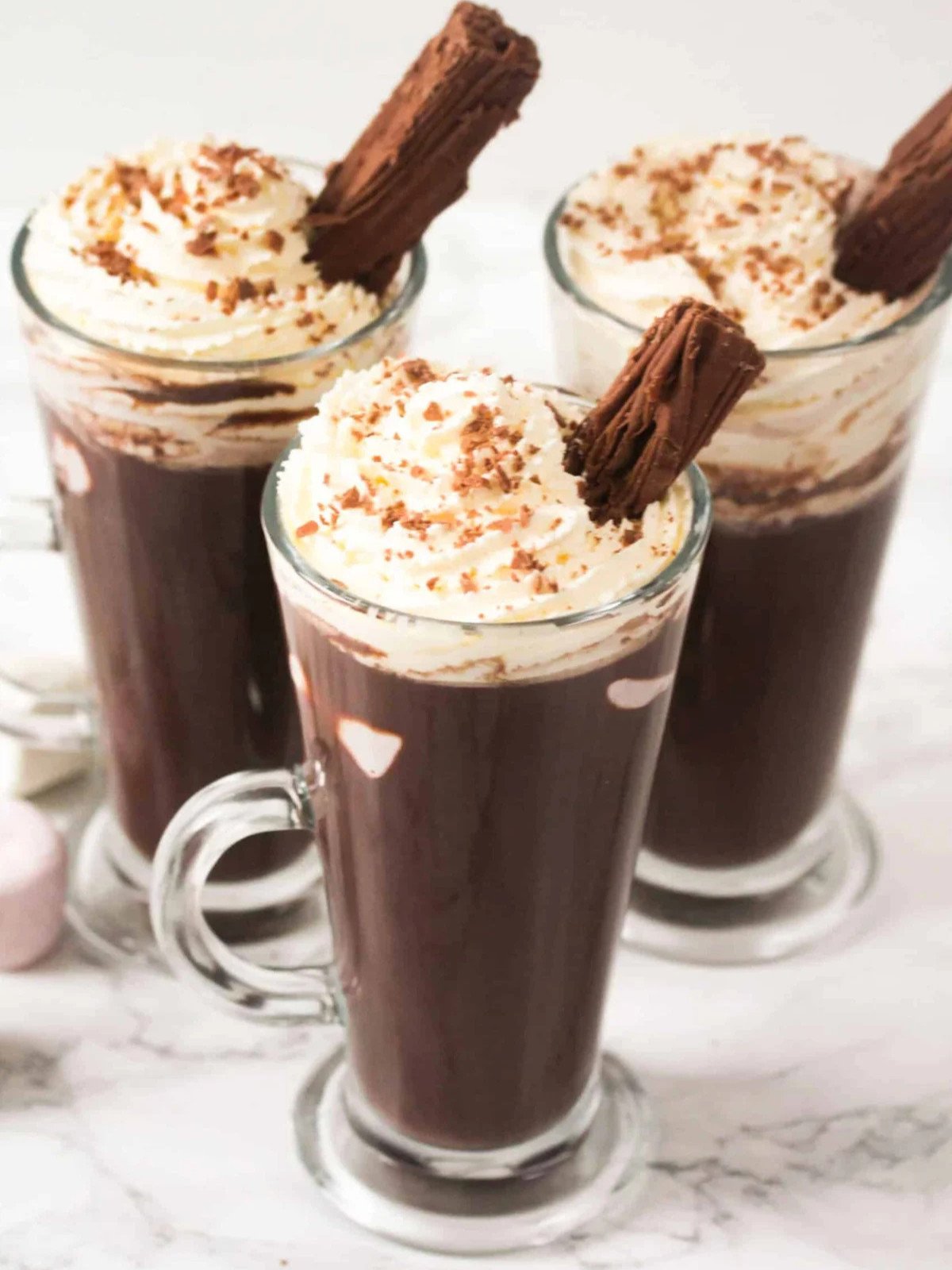 Hot chocolate drink in three glass cups topped with whipped cream, marshmallows and a chocolate flake.