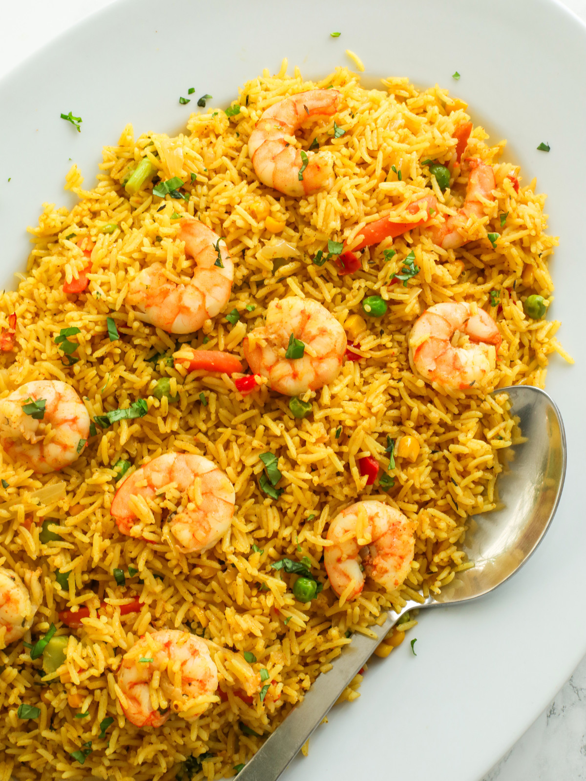 Nigerian fried rice in a white oval plate with a silver spoon.