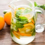 Oranges slices, mint leaves, ice and water in a glass jar. Oranges and glass cup on a brown table .