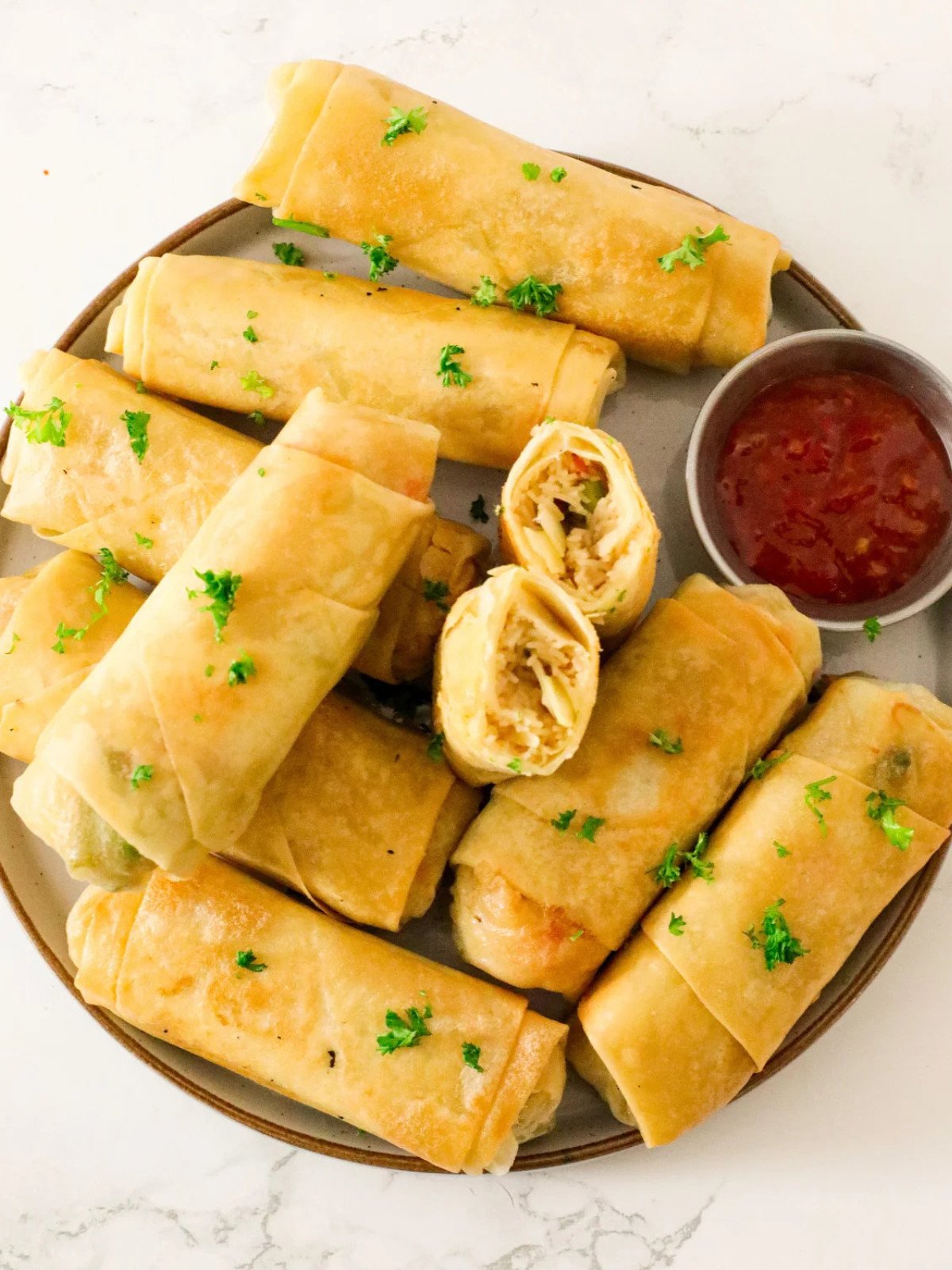 Spring rolls in a plate topped with parsley and sweet chili sauce.