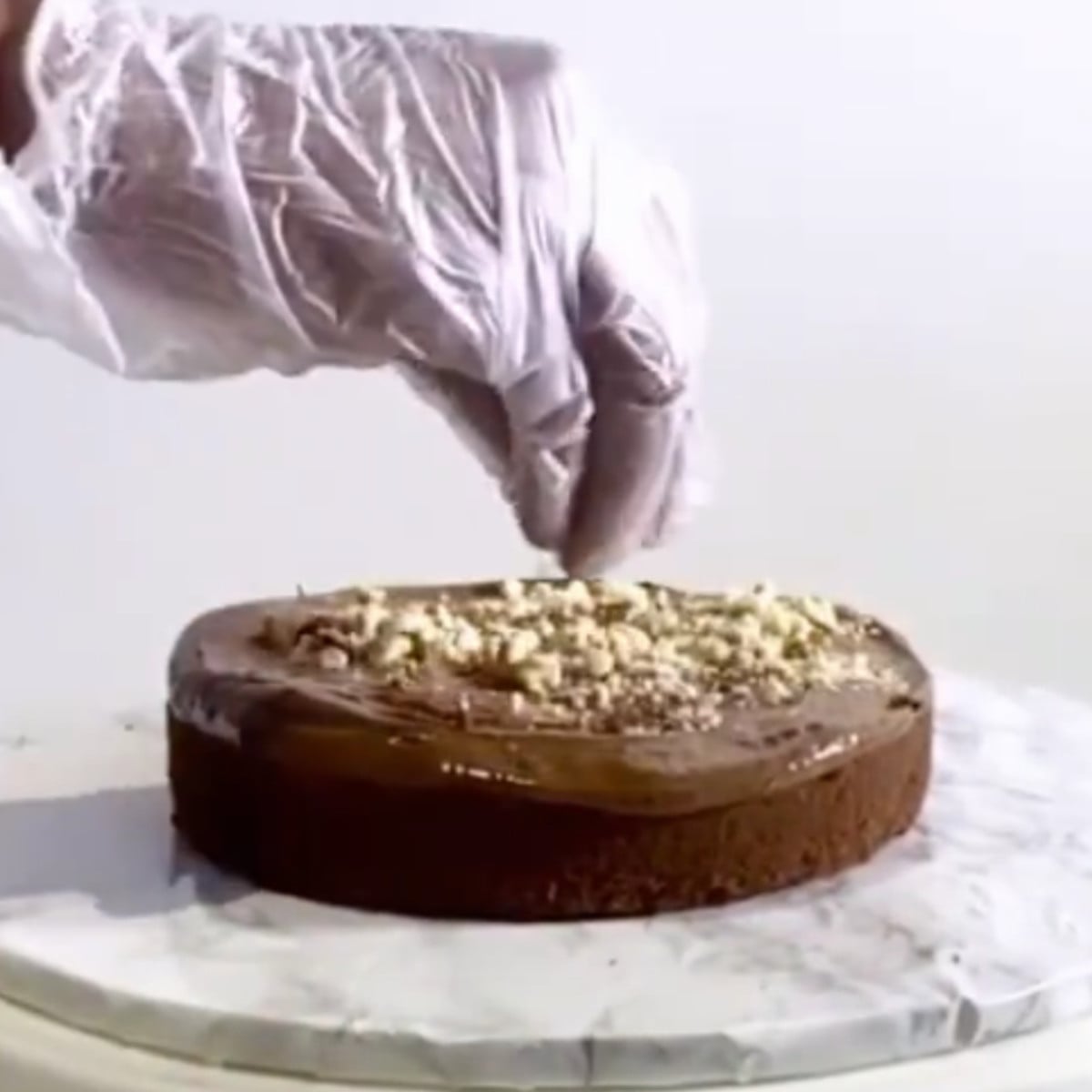 Chocolate cake with a layer of chocolate ganache and crushed hazelnuts on a cake board.