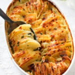 Dauphinoise in a white oval shaped dish with a large silver spoon.