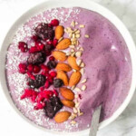 Blackberries, frozen bananas and sweetener blended in a bowl with almonds and seeds in a white bowl.