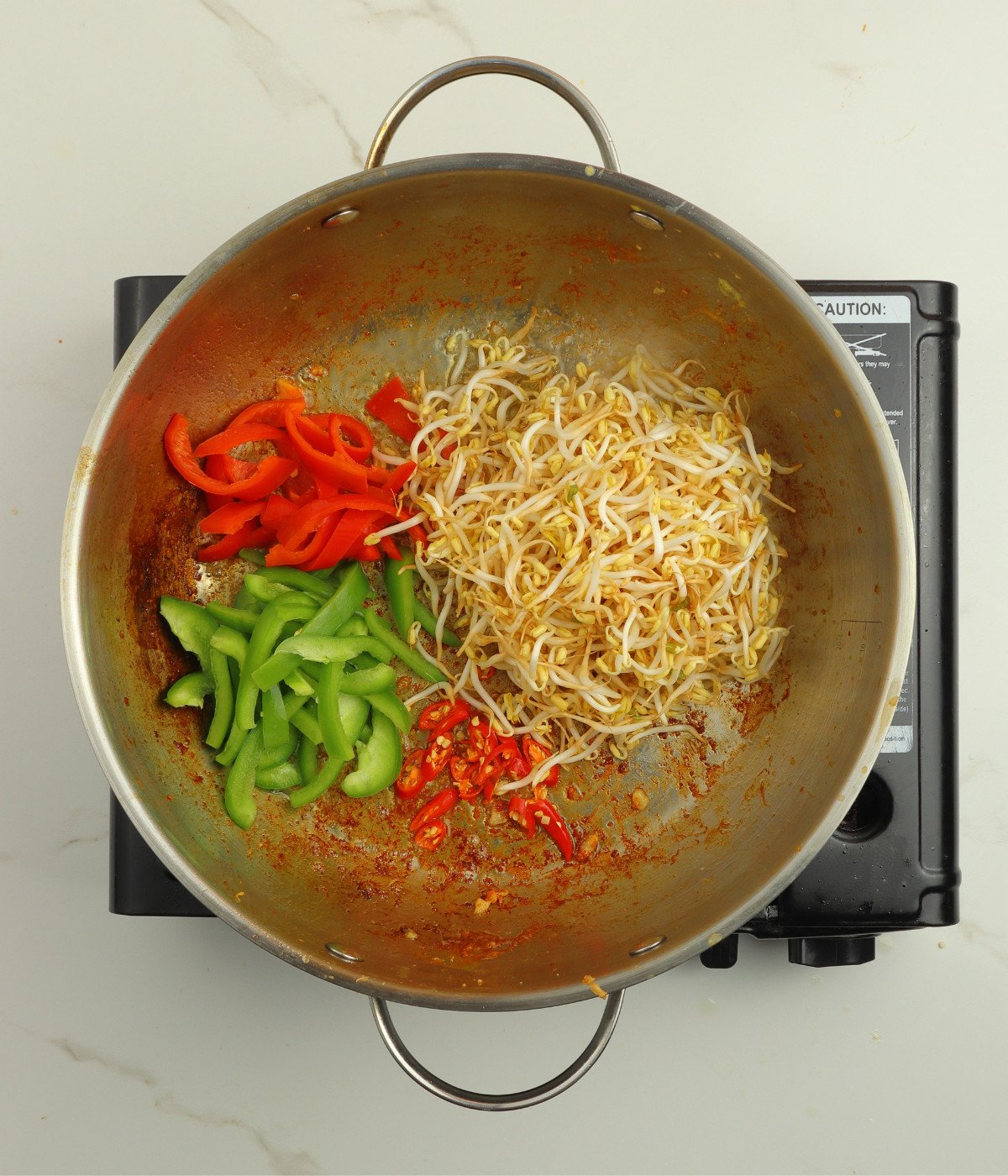 Capsicum peppers, bean sprouts and chillies cooking in a silver wok.
