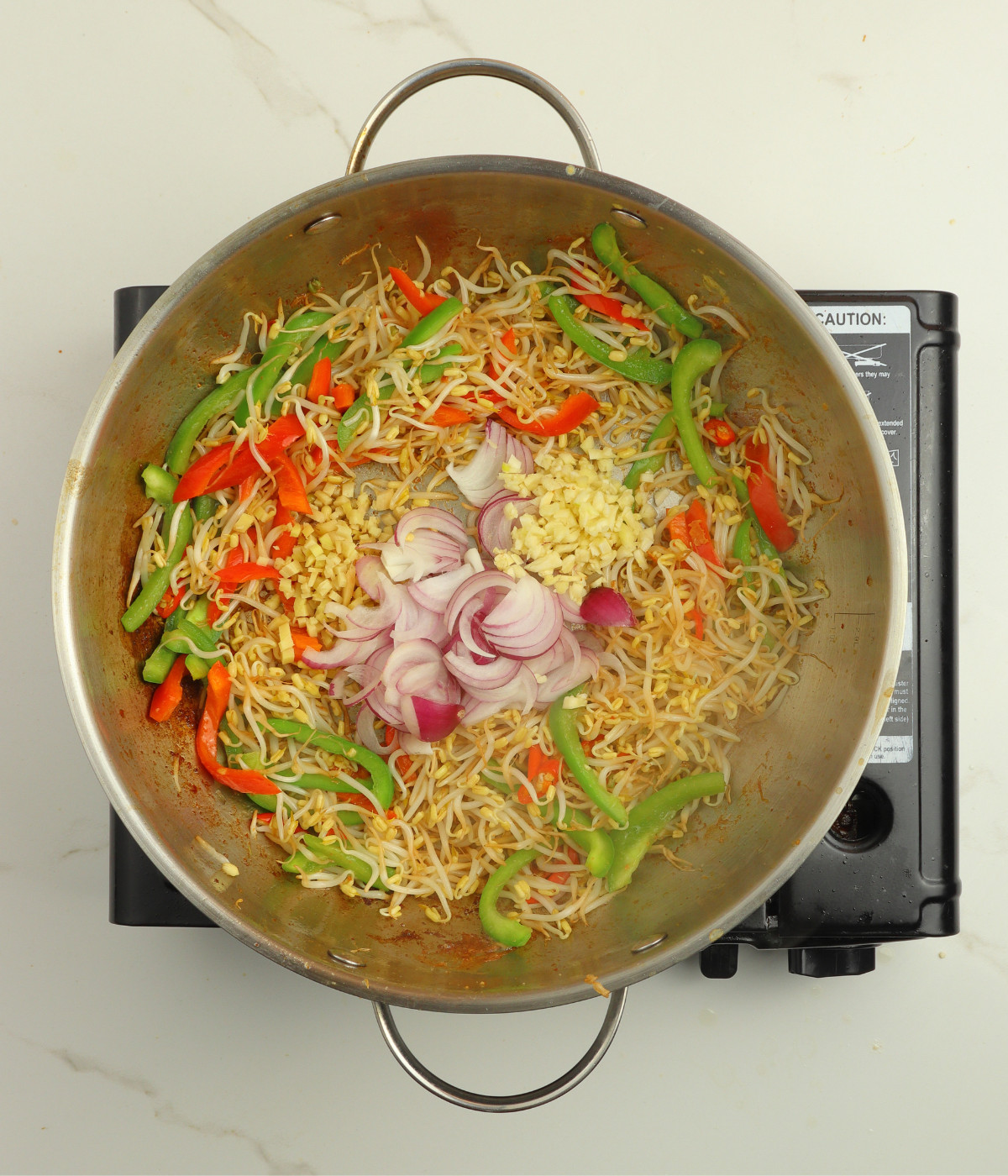 Capsicum peppers, bean sprouts, onions, ginger and garlic and chillies cooking in a silver wok.