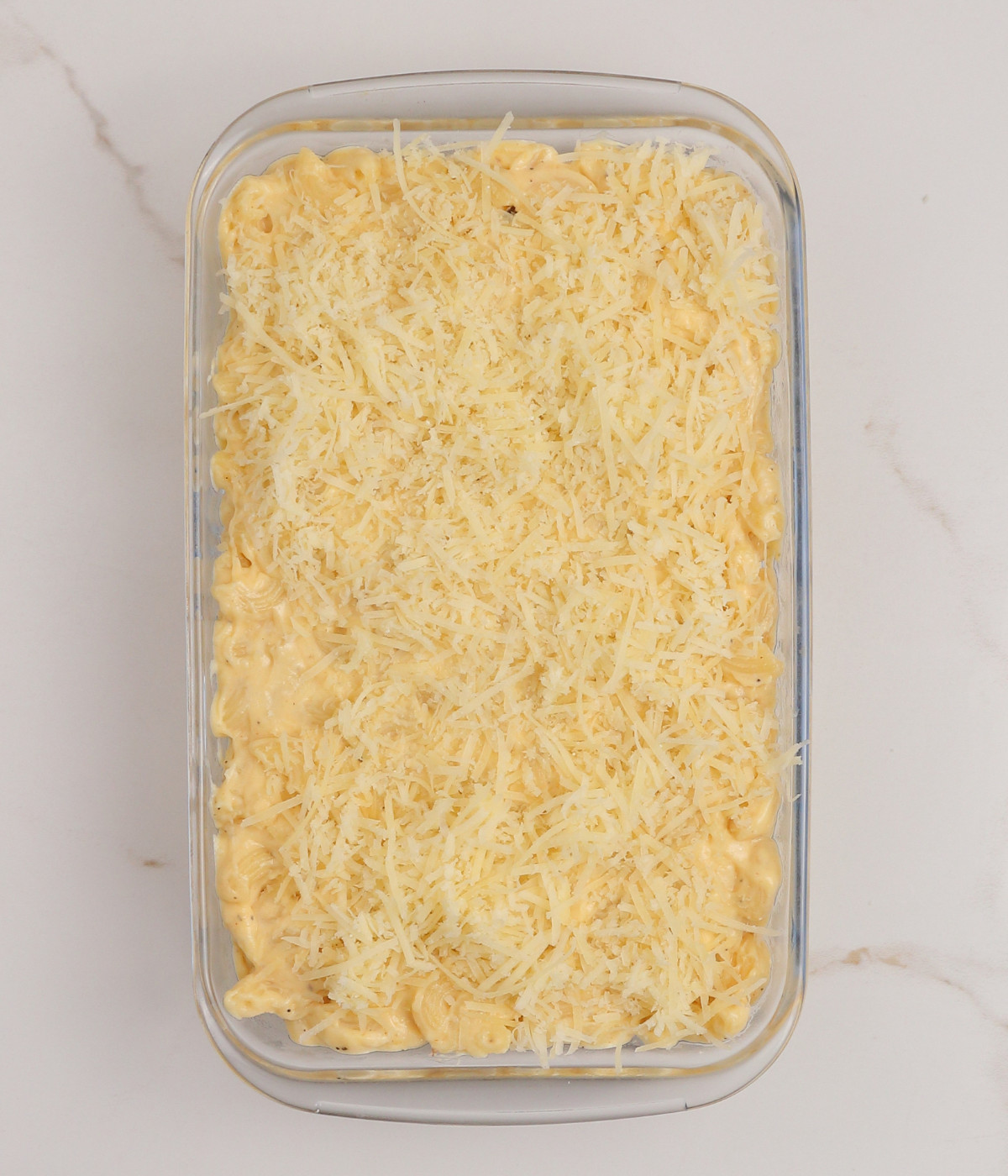 Cheesy macaroni pasta topped with shredded cheese in a glass rectangle dish.