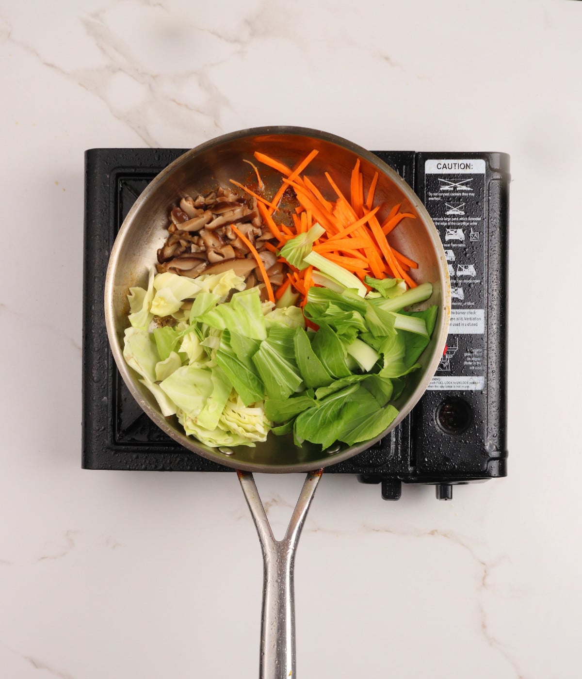 Mushrooms, carrots, cabbage and pak choi cooking in a pan.