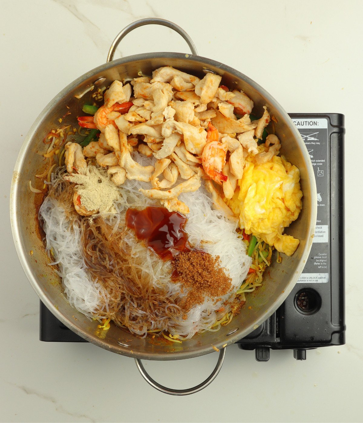 Noodles, sauce, vegetables, chicken and shrimp cooking in a silver wok.