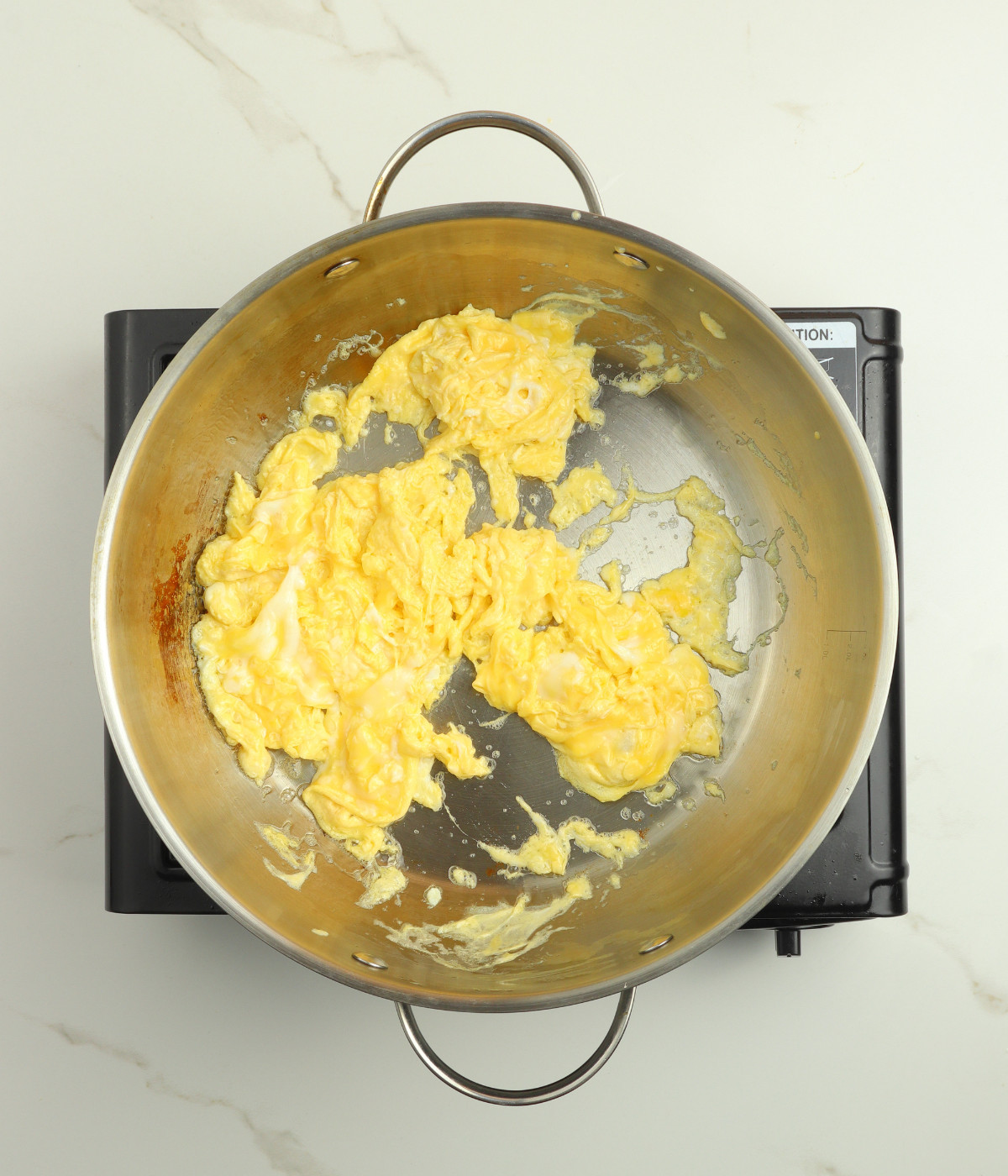 Scrambled eggs cooked in a silver wok.