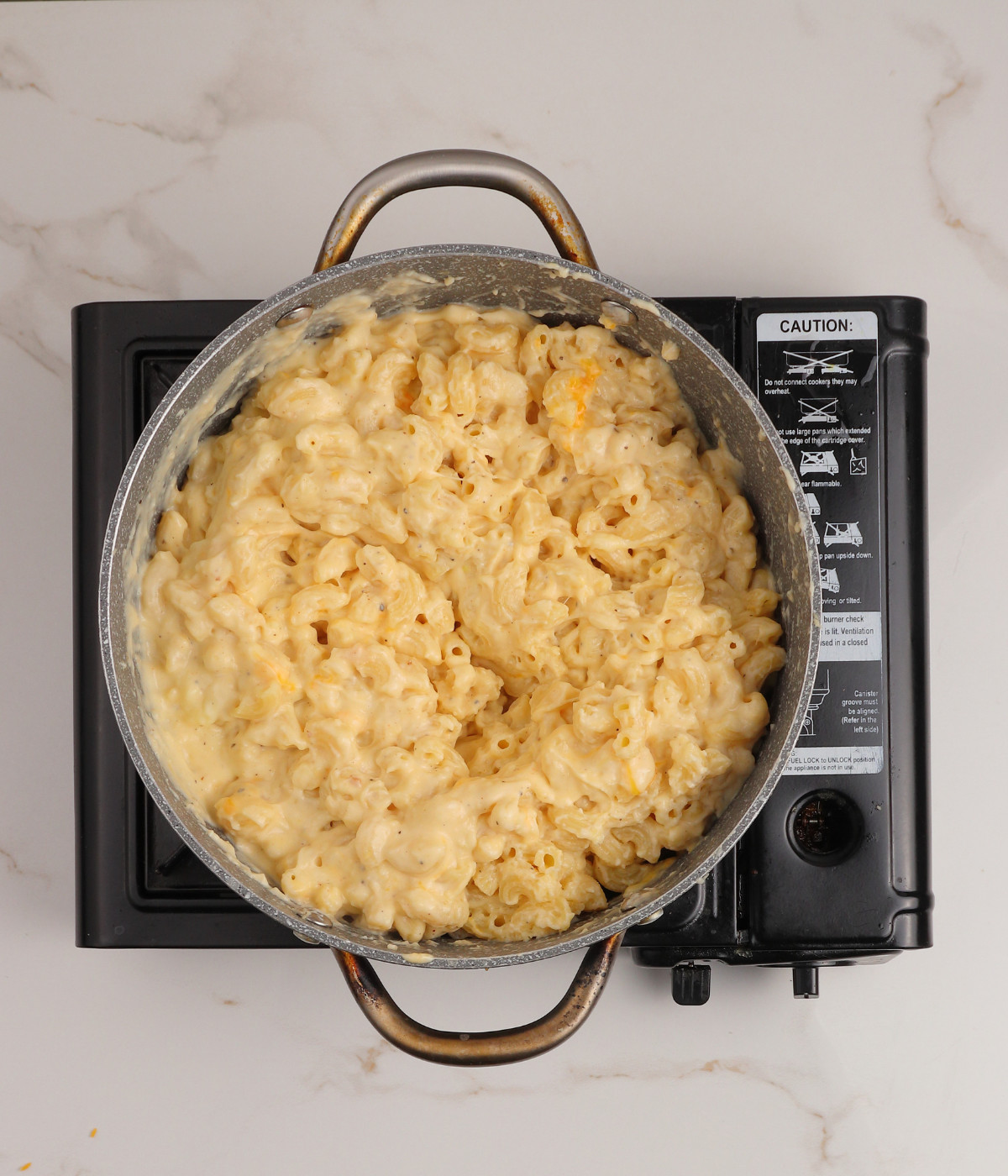 Seasoned roux mixed with half cooked elbow pasta and cheese in a pot.