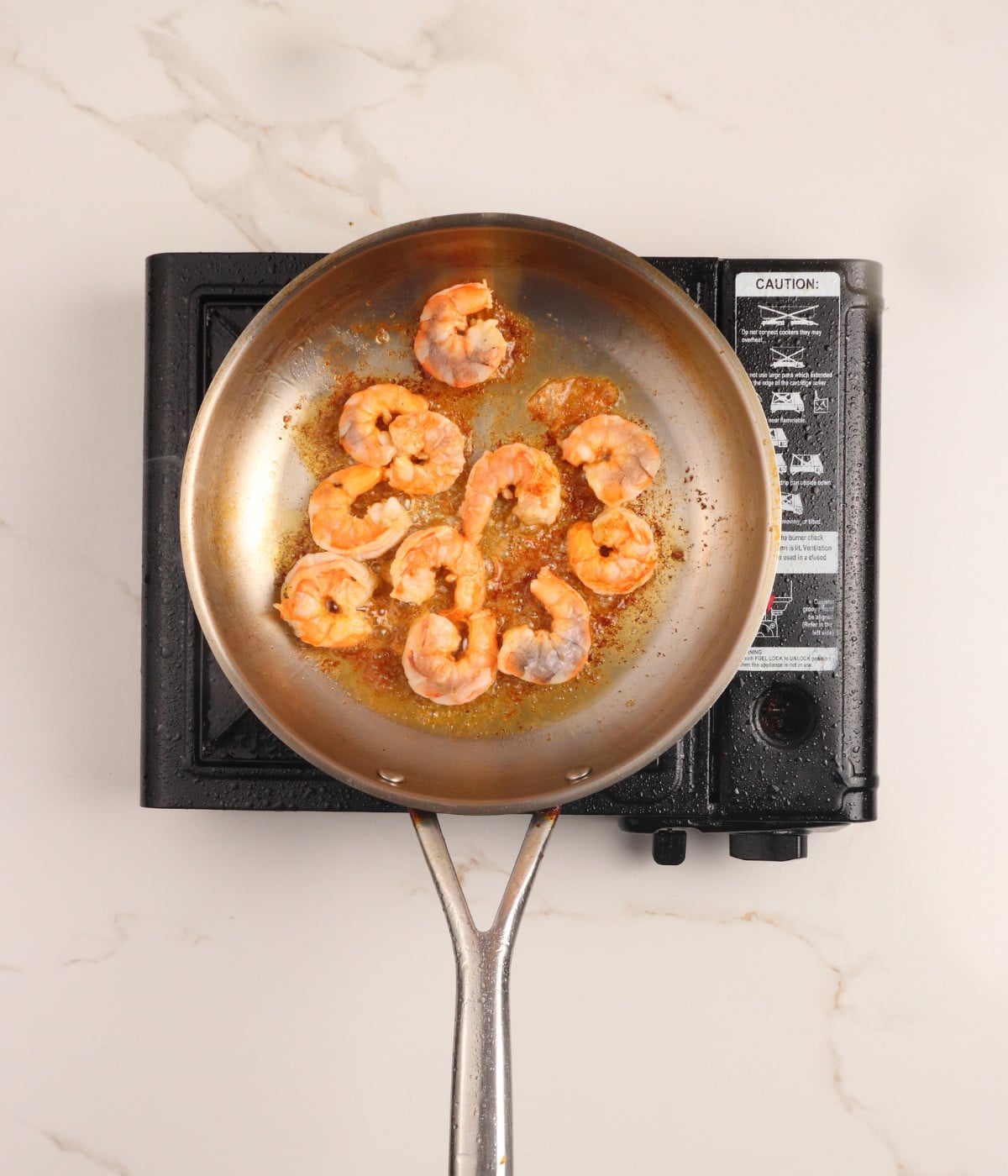 Seasoned shrimp cooking in a silver pan.