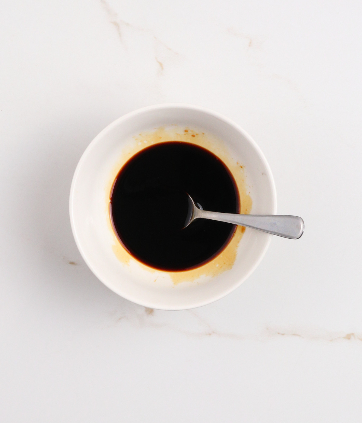 Soy sauce, mirinm and brown sugar mixed in a white bowl with a silver spoon.