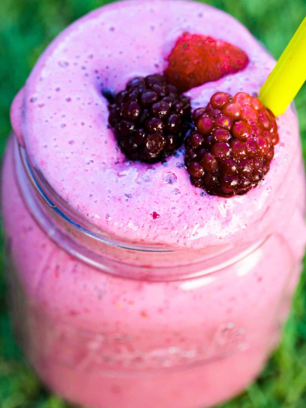 Strawberries and blackberry smoothie in a jar with a yellow straw.