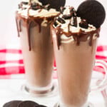Two oreo drinks in a dessert cup with whipped cream and oreos.