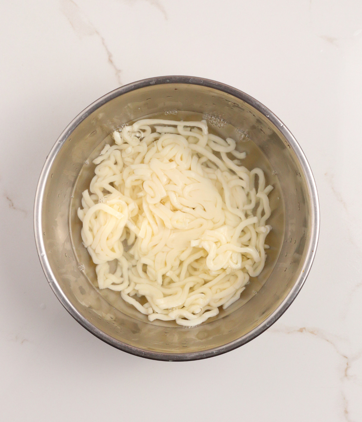 Udon noodles and water in a silver bowl.
